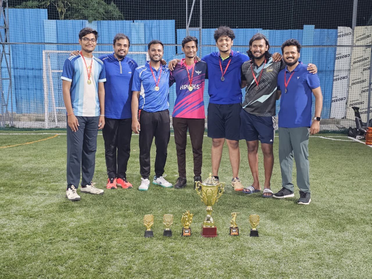 The Cricket Clash champions with medals and the winners' trophy on the turf