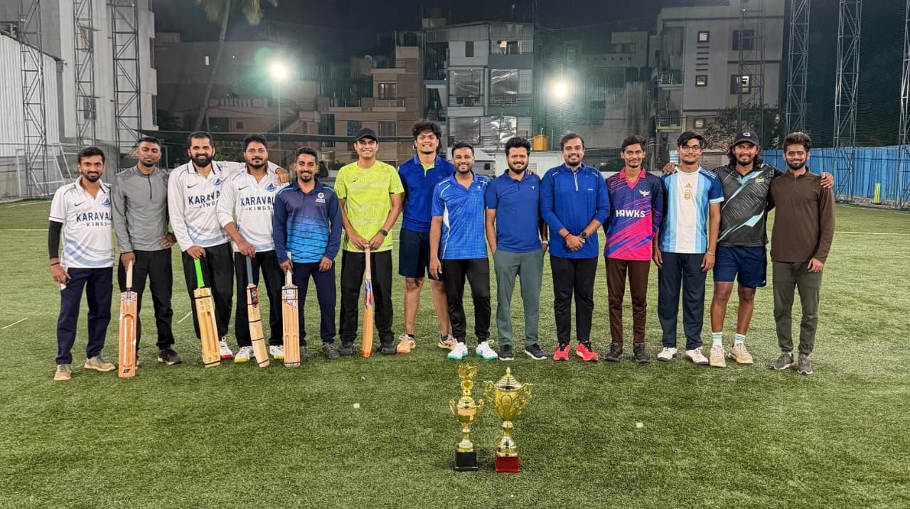 Both Cricket Clash teams lined up on the floodlit turf with bats and trophies