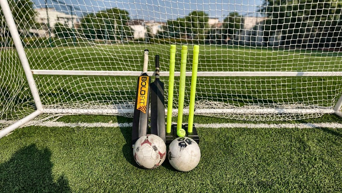Cricket bats, wickets, ball and footballs in front of a goal